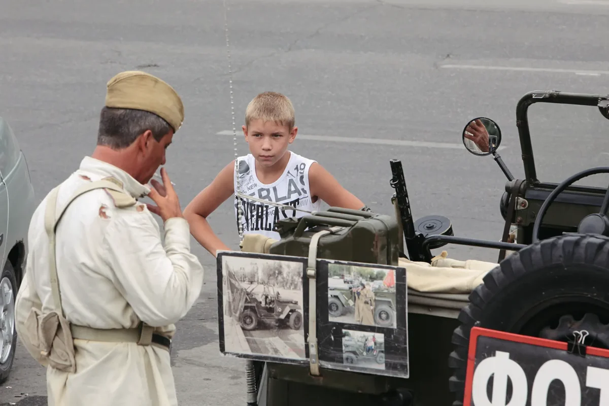 A boy looks at a staged war relic display—history reduced to a roadside attraction.