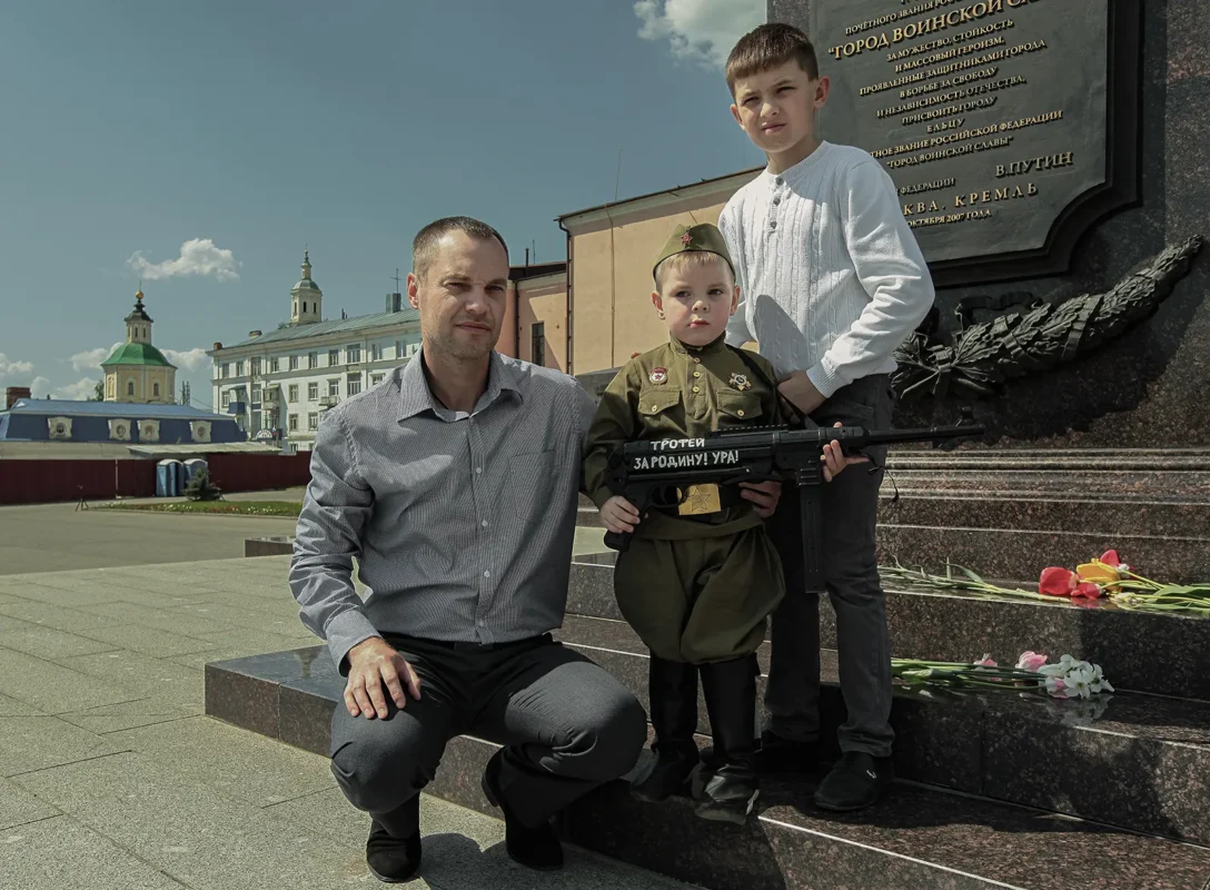 A family of collectors of Soviet memorabilia with a six-year-old boy dressed in a 1940s Soviet military uniform. Inscription on the wooden rifle: “Trophy for the Motherland! Hurrah!” In the background, a stele bearing Putin’s words awarding Yelets the title of “City of Military Glory.”